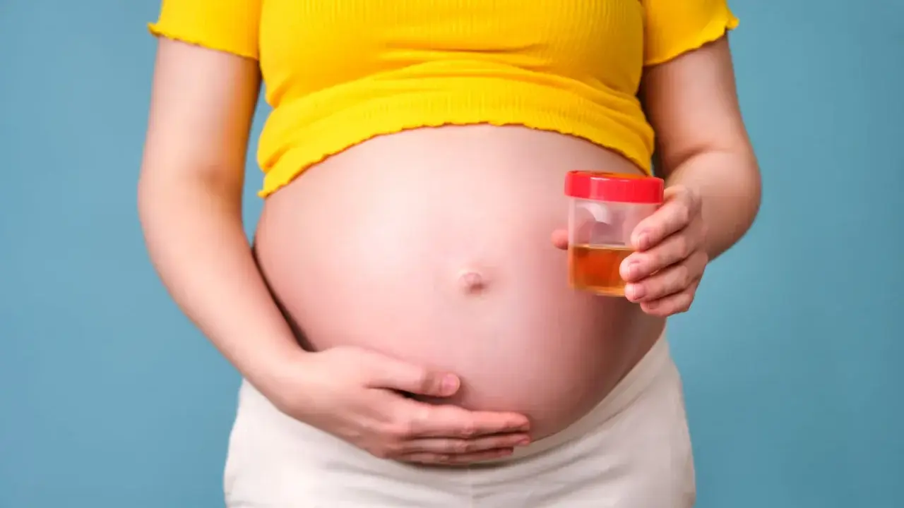 Kobieta w ciąży trzyma pojemnik z próbką moczu, badanie na obecność ketonów w moczu w ciąży.