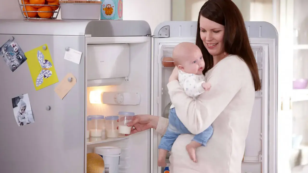 Mama z dzieckiem przy lodówce, gdzie przechowywanie mleka matki jest łatwe dzięki specjalnym pojemnikom.