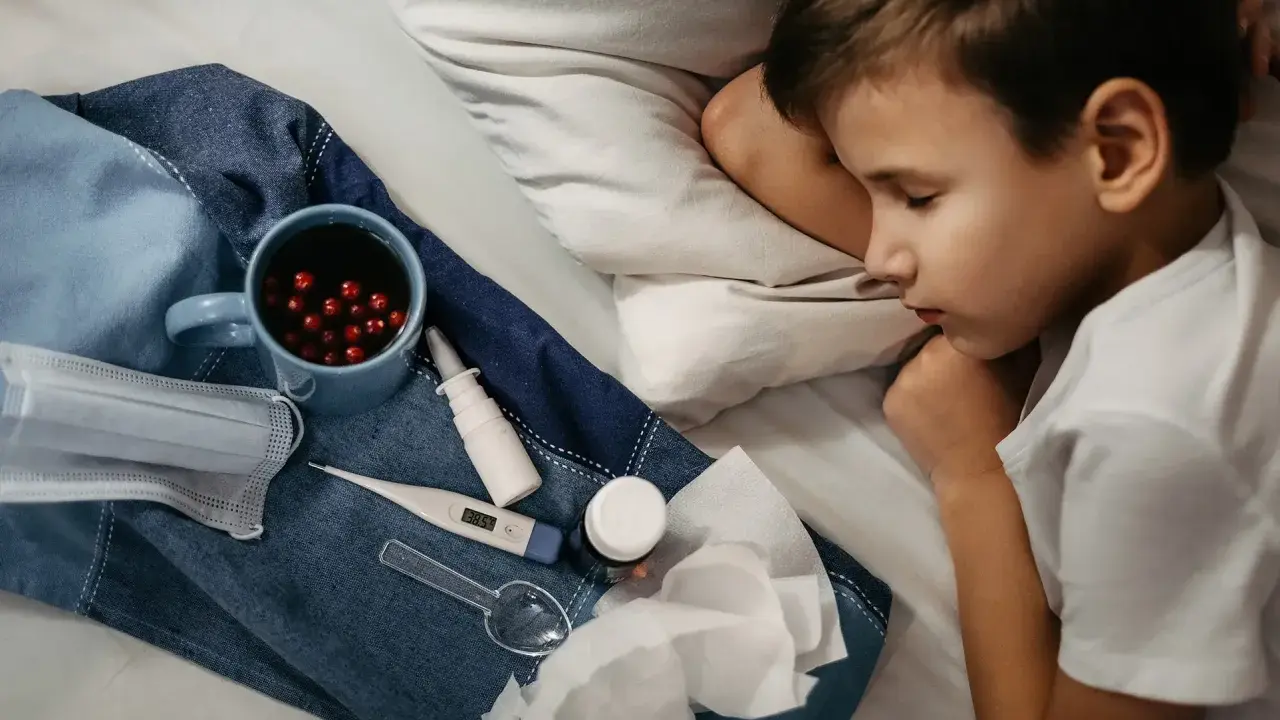 Chory chłopiec śpi, obok kubek z naparem, termometr, maska i chusteczki. To objawy grypy A.