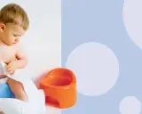 Małe dziecko siedzi na niebieskim nocniku, trzymając rolkę papieru toaletowego. Jak nauczyć dziecko korzystać z nocnika?