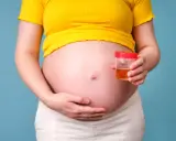 Kobieta w ciąży trzyma pojemnik z próbką moczu, badanie na obecność ketonów w moczu w ciąży.