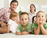 Uśmiechnięta rodzina z czwórką dzieci. Widać, ile jest rodzinnego na dziecko, gdy wszyscy razem leżą na dywanie.