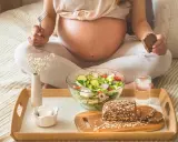 Ciężarna kobieta je zdrową sałatkę i chleb. To przykład, co jeść w ciąży, dbając o siebie i dziecko.
