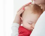 Ciemiączko przednie niemowlęcia delikatnie dotykane przez matkę. Dziecko śpi wtulone w jej ramię.