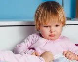 Smutna dziewczynka w różowej bluzce, być może z powodu nietolerancji laktozy, siedzi w łóżku.