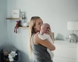 Mama tuli noworodka, który ma czkawkę. W tle pokój dziecięcy z pluszakami.