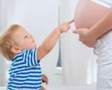 Mały chłopiec w pasiastej koszulce dotyka paluszkiem brzucha mamy, która jest w 25 tygodniu ciąży.