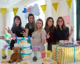 Pięć uśmiechniętych kobiet świętuje baby shower. Na stole tort z pieluch, prezenty i słodkości. To radosne wydarzenie, co to jest baby shower, pełne miłości i oczekiwania.