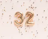 Złote balony z cyframi 3 i 2, otoczone konfetti. To już 32 tydzień ciąży, czas na świętowanie!