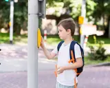 Chłopiec z plecakiem naciska przycisk na przejściu dla pieszych. Od ilu lat dziecko może samo chodzić po mieście?