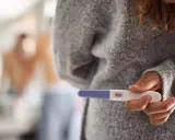 Kobieta trzyma test ciążowy z dwoma kreskami. Czy to oznacza, że dni niepłodne to już przeszłość?