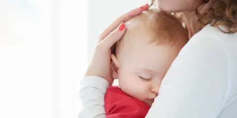 Ciemiączko przednie niemowlęcia delikatnie dotykane przez matkę. Dziecko śpi wtulone w jej ramię.
