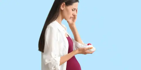 Kobieta w ciąży z bólem głowy i krwią z nosa, trzymająca w ręku coś owiniętego w papier.