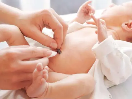 Delikatne czyszczenie kikuta pępowiny noworodka. Dłoń rodzica ostrożnie dotyka małego brzuszka, by zadbać o higienę.