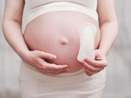 Ciężarna kobieta trzyma podpaskę, sugerując pytanie: czy w okres można zajść w ciążę?