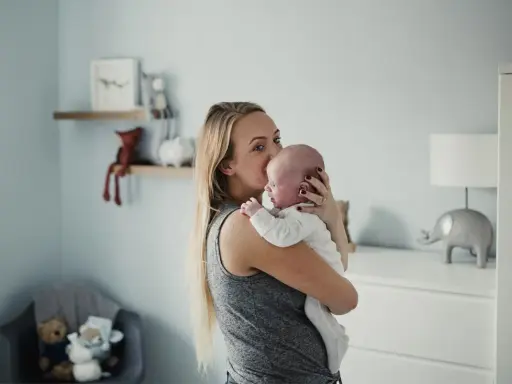 Mama tuli noworodka, który ma czkawkę. W tle pokój dziecięcy z pluszakami.