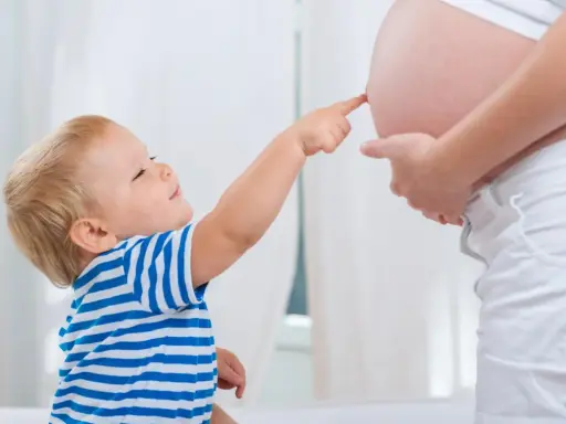 Mały chłopiec w pasiastej koszulce dotyka paluszkiem brzucha mamy, która jest w 25 tygodniu ciąży.