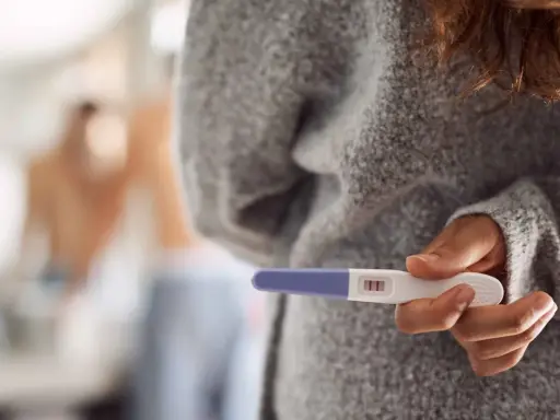 Kobieta trzyma test ciążowy z dwoma kreskami. Czy to oznacza, że dni niepłodne to już przeszłość?