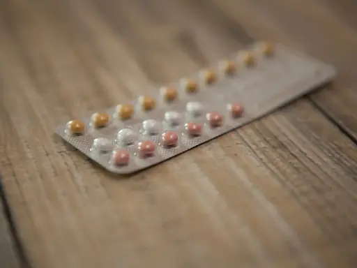 Opakowanie tabletek antykoncepcyjnych z różowymi, białymi i żółtymi pigułkami na drewnianym tle.