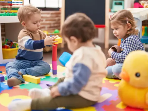 Trójka małych dzieci bawi się klockami i zabawkami na kolorowej macie w żłobku.