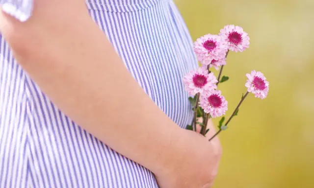 Delikatne kwiaty w dłoni na tle sukienki w paski. To początek pięknej podróży, może właśnie 3 tydzień ciąży.