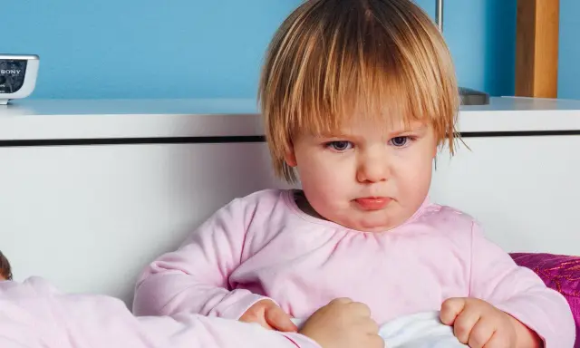 Smutna dziewczynka w różowej bluzce, być może z powodu nietolerancji laktozy, siedzi w łóżku.