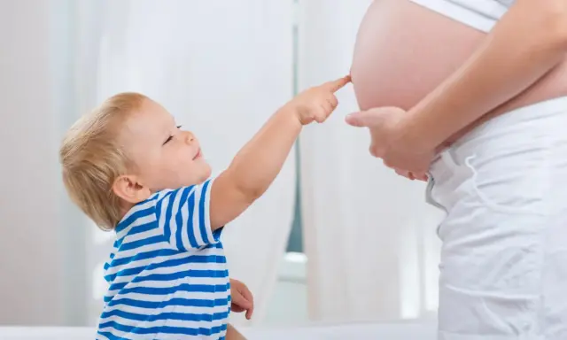Mały chłopiec w pasiastej koszulce dotyka paluszkiem brzucha mamy, która jest w 25 tygodniu ciąży.