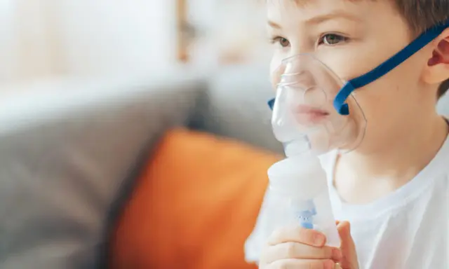 Chłopiec z maską inhalacyjną na twarzy, korzystający z nebulizatora. Pomaga mu to w leczeniu kataru.