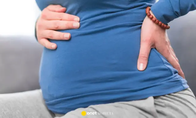 Ciężarna kobieta trzyma się za brzuch i plecy, odczuwając dyskomfort. To może być objaw biegunki przed porodem.