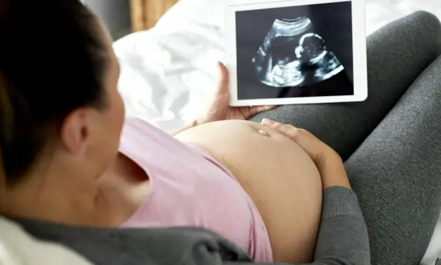 Kobieta w ciąży ogląda na tablecie zdjęcie USG. To jej badania prenatalne w 3 trymestrze.