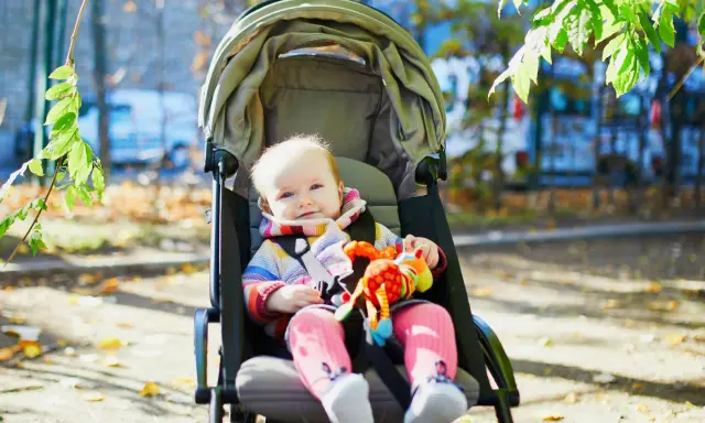 Uśmiechnięte dziecko w kolorowym sweterku i różowych skarpetkach siedzi w spacerówce, trzymając zabawkę. Od kiedy spacerówka stała się jego ulubionym miejscem na świecie.