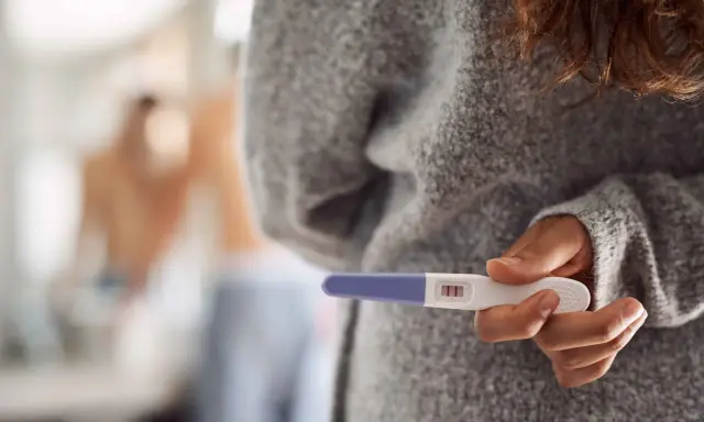 Kobieta trzyma test ciążowy z dwoma kreskami. Czy to oznacza, że dni niepłodne to już przeszłość?