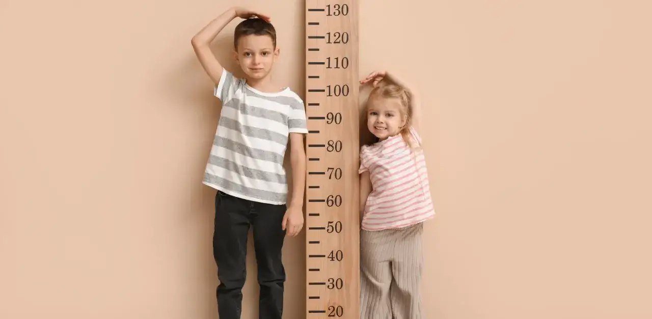 Chłopiec i dziewczynka mierzą wzrost. Chłopiec ma ok. 105 cm, dziewczynka ok. 92 cm. Jaki wiek pasuje do rozmiaru 92?