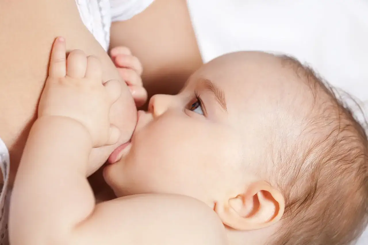 Malutkie rączki dziecka obejmujące pierś mamy, czułe karmienie. Zastój w piersi to wyzwanie, ale miłość i bliskość pokonają wszystko.