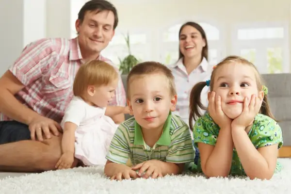 Uśmiechnięta rodzina z czwórką dzieci. Widać, ile jest rodzinnego na dziecko, gdy wszyscy razem leżą na dywanie.