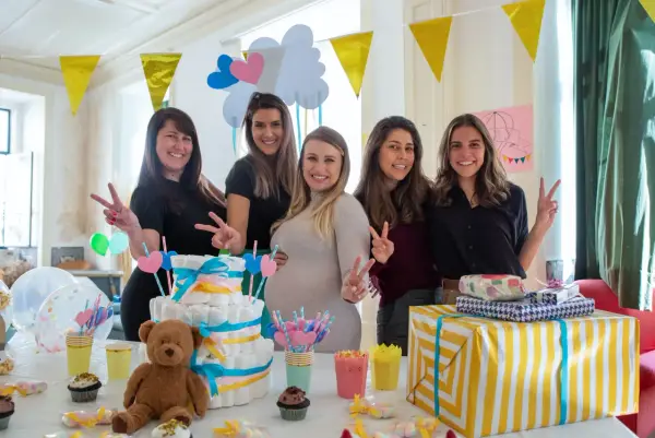 Pięć uśmiechniętych kobiet świętuje baby shower. Na stole tort z pieluch, prezenty i słodkości. To radosne wydarzenie, co to jest baby shower, pełne miłości i oczekiwania.