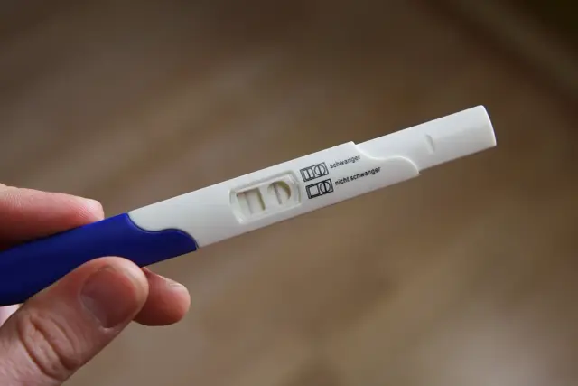 Dłoń trzyma test ciążowy. Widoczne są dwie kreski, co oznacza, że test ciążowy negatywny.