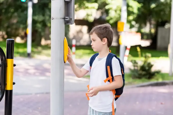 Chłopiec z plecakiem naciska przycisk na przejściu dla pieszych. Od ilu lat dziecko może samo chodzić po mieście?